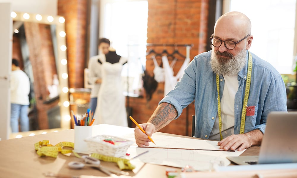 Tailor working on garment designs at table in clothing studio