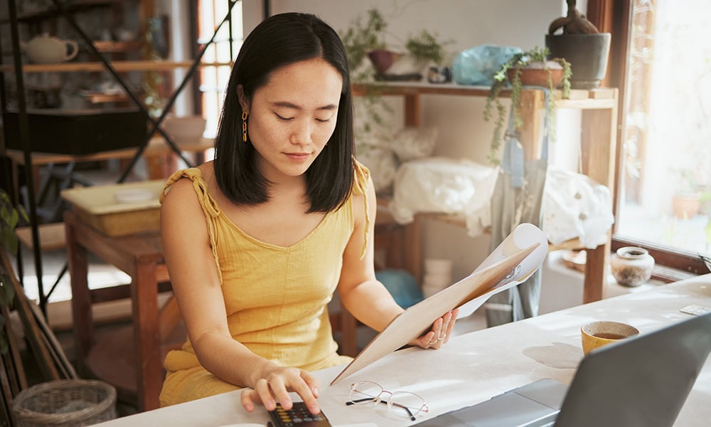 Entrepreneur calculating expenses while reviewing paperwork in creative workspace