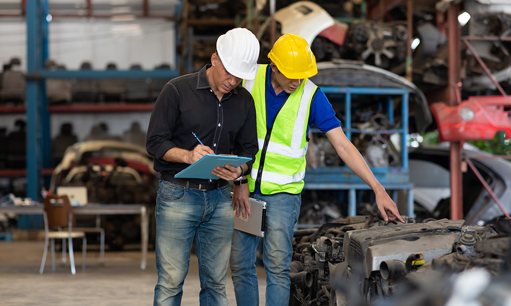 Two industrial workers wearing hard hats reviewing machinery in manufacturing facility